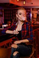 Young pretty woman smoke an electronic cigarette at the vape bar photo