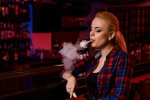 Young pretty woman smoke an electronic cigarette at the vape bar photo