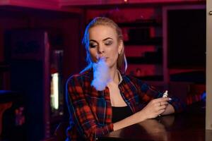 Young pretty woman in a shirt in a cage smoke an electronic cigarette at the vape bar photo