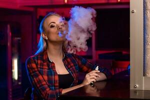Young pretty woman in a shirt in a cage smoke an electronic cigarette at the vape bar photo
