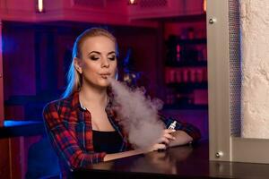 Young pretty woman in a shirt in a cage smoke an electronic cigarette at the vape bar photo