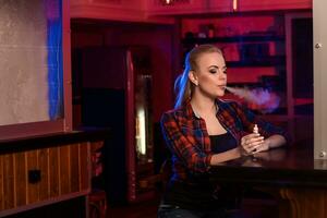 Young pretty woman in a shirt in a cage smoke an electronic cigarette at the vape bar photo