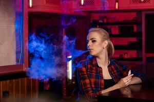 Young pretty woman in a shirt in a cage smoke an electronic cigarette at the vape bar photo