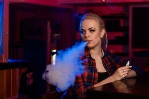 joven bonito mujer en un camisa en un jaula fumar un electrónico cigarrillo a el vape bar foto