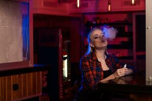 Young pretty woman in a shirt in a cage smoke an electronic cigarette at the vape bar photo