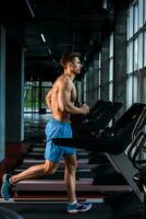 Side view full length of young man in sportswear running on treadmill at gym photo