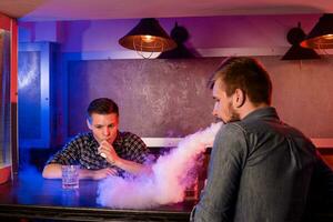 Two young men smoke electronic cigarettes in a vapebar photo