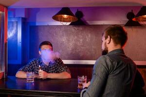 Two young men smoke electronic cigarettes in a vapebar photo