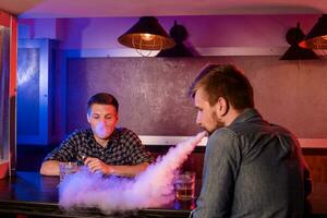 Two young men smoke electronic cigarettes in a vapebar photo