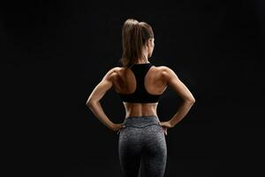 Shot of a strong woman with muscular abdomen in sportswear. Fitness female model posing on black background. photo