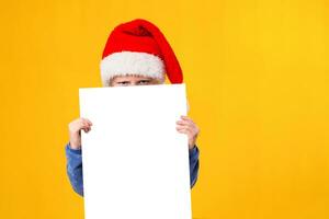 linda pequeño niña en Papa Noel claus sombrero con un blanco blanco papel hoja. Navidad, Navidad, nuevo año, invierno, gente, anuncio publicitario, rebaja concepto. foto