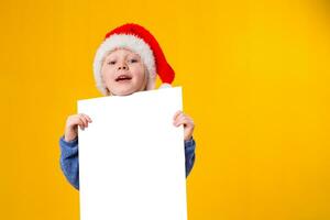 Cute little girl in Santa Claus hat with a white blank paper sheet. Christmas, x-mas, New Year, Winter, people, advertisement, sale concept. photo