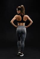 Shot of a strong woman with muscular abdomen in sportswear. Fitness female model posing on black background. photo