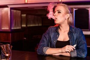 joven bonito mujer fumar un electrónico cigarrillo a el vape bar foto