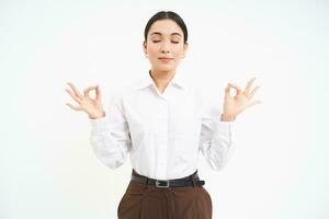 Wellbeing and workplace. Young asian businesswoman meditates, keeps calm, relaxes after work, white background photo