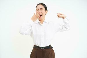 Tired asian corporate woman, yawns and stretches her back from fatigue after work, isolated on white background photo