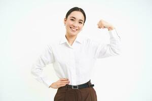 negocio y corporativo mujer. fuerte y exitoso asiático mujer emprendedor, muestra bíceps, flexionando músculos, sonriente complacido, blanco antecedentes foto