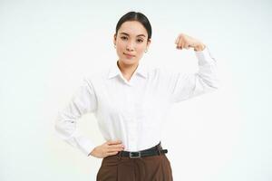 confidente asiático mujer de negocios, flexionando bíceps, muestra fuerte músculo con grave y seguro de sí mismo rostro, blanco antecedentes foto