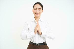 Smiling calm young woman, holds hands in pray with eyes closed, makes wish, hopes for smth, white background photo