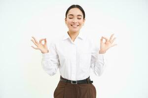 Wellbeing and workplace. Young asian businesswoman meditates, keeps calm, relaxes after work, white background photo