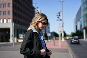 Portrait of corporate woman in suit and sunglasses, standing on street, looking confident and relaxed photo