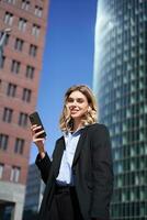 Portrait of successful businesswoman having a telephone conversation in wireless headphones, walking on street. Corporate woman with smartphone in city center photo