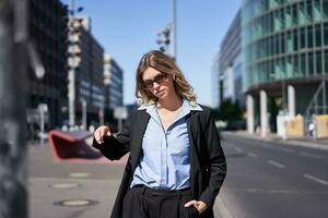 Portrait of confident corporate woman, young saleswoman in suit and sunglasses, looking self-assured on city street photo