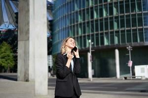 Pleased businesswoman celebrates on street, talking on mobile phone, receive good news on call photo