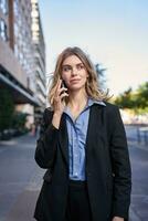 Vertical shot of confident young businesswoman making phone call, standing on street and talking on telephone photo