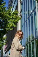 Portrait of confident saleswoman going to work, wearing sunglasses and suit. Businesswoman on her way to office, posing outdoors photo