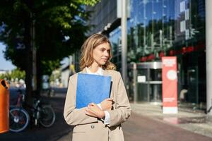 trabajo y corporativo gente. confidente mujer de negocios participación un azul carpeta con negocio documentos, caminando en calle foto