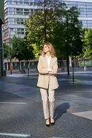Portrait of young confident corporate woman in beige suit, standing on street in her business outfit, looking self-assured photo