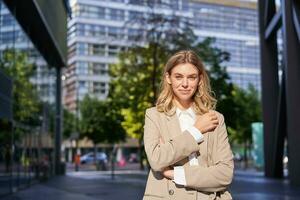 Stylish corporate woman, young lady boss in suit, looking confident and happy, posing outdoors on street photo