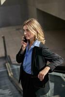 Portrait of corporate woman standing on escalator, making a phone call, using smartphone, walking in city photo