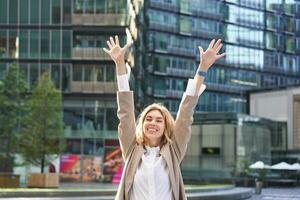 corporativo mujer celebrando su victoria fuera de en calle. contento mujer de negocios levantamiento manos arriba y triunfando desde emoción foto