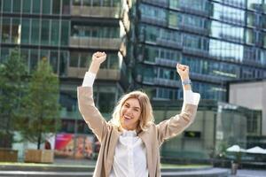 corporativo mujer celebrando su victoria fuera de en calle. contento mujer de negocios levantamiento manos arriba y triunfando desde emoción foto