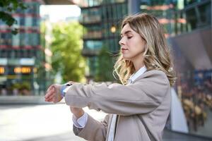 cerca arriba retrato de mujer de negocios mirando a su digital reloj mientras esperando para alguien afuera. corporativo mujer leyendo mensaje en su muñeca dispositivo foto