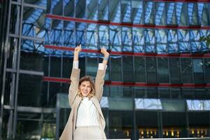 Happy businesswoman dancing on street, raising hands up. Corporate woman celebrates her victory or success photo