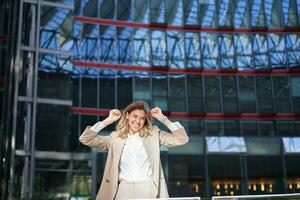 Excited young businesswoman celebrating, triumphing, feeling free and happy, posing in the city near office buildings photo