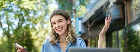 Vertical shot of smiling successful businesswoman, using digital tablet, sitting outdoors in park, working with laptop. Coporate people concept photo