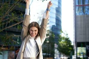 Saleswoman expresses joy and happiness. Businesswoman triumphing on street, raising hands up, celebrating victory, smiling pleased photo