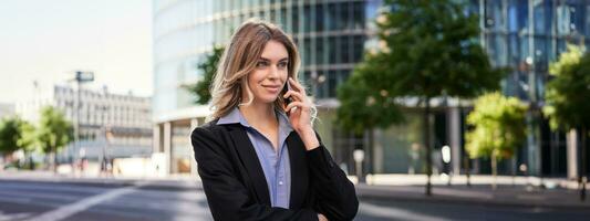 Portrait of successful businesswoman, company ceo walks on street and makes phone calls, talking on smartphone photo