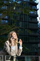 Vertical shot of businesswoman on a call, standing outside business center, talking on mobile phone photo