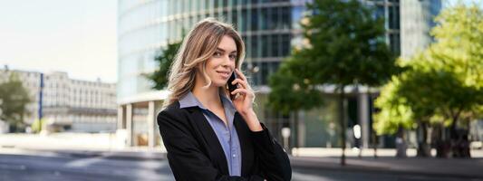 Portrait of successful businesswoman, company ceo walks on street and makes phone calls, talking on smartphone photo