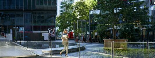 Businesswoman in suit, walking in city, going to work with laptop and documents. Corporate people concept photo