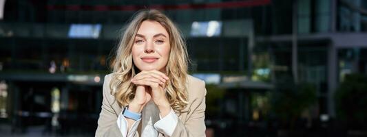 hermosa corporativo mujer, mira soñador y sonrisas, soportes fuera de en calle, se inclina su cabeza en manos, soñador, descansando en descanso después oficina trabajo foto