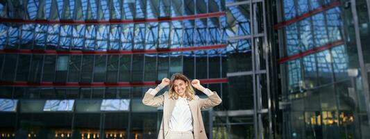 Excited young businesswoman celebrating, triumphing, feeling free and happy, posing in the city near office buildings photo