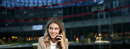 Vertical shot of smiling businesswoman answer mobile phone call, talking on smartphone and drinking coffee photo