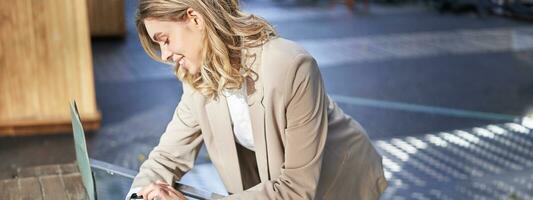 Portrait of businesswoman looks at her digital watch to check time, standing outside on street near office photo