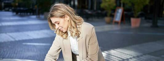 Portrait of businesswoman looks at her digital watch to check time, standing outside on street near office photo